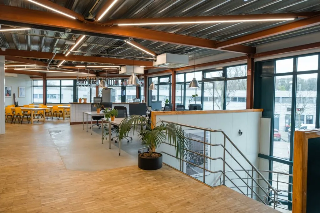 Moderne kantoorruimte aan de Johan van Hasseltweg met open werkplekken, gele eetkamerstoelen en grote ramen voor natuurlijk licht.